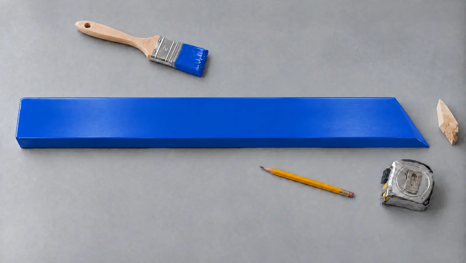 A pine board painted royal blue next to a brush, pencil and tape measure
